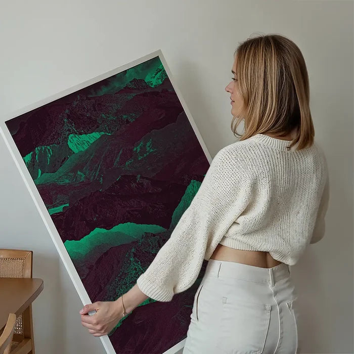 Woman holding a large abstract mountain print with deep green and purple hues on thick art paper.