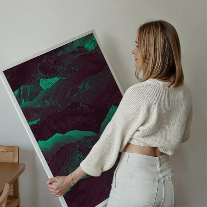 Woman holding a large abstract mountain print with deep green and purple hues on thick art paper.