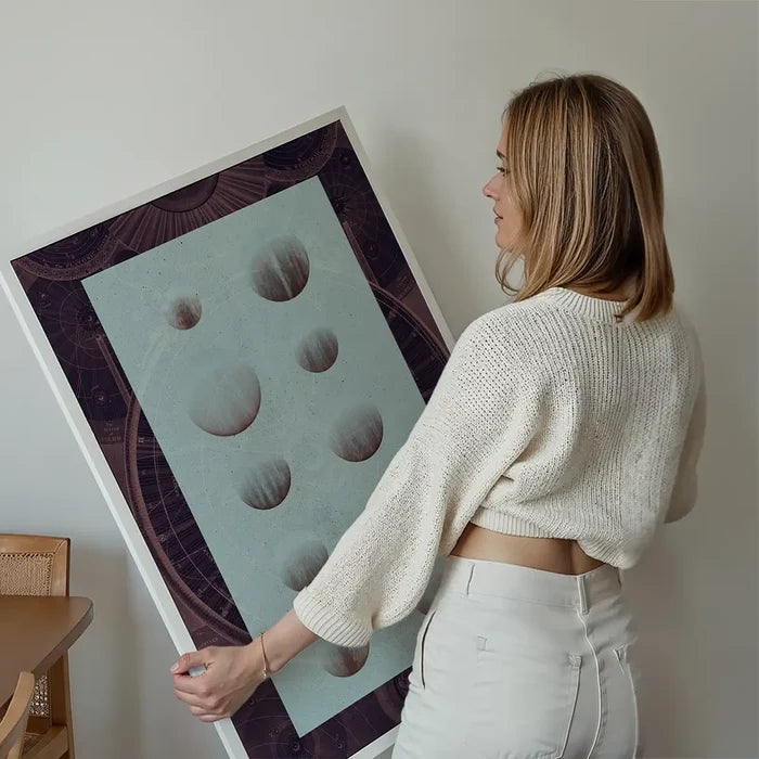 Woman holding a dark astrology chart print with vintage space diagrams and planets on light blue.