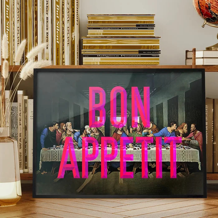 Black framed "Bon Appetit" typography print over a Last Supper painting, on a wooden shelf.