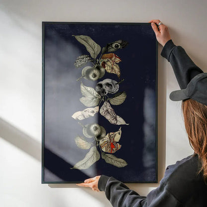 Navy botanical skull print on archival art paper, held by hands against a white wall.