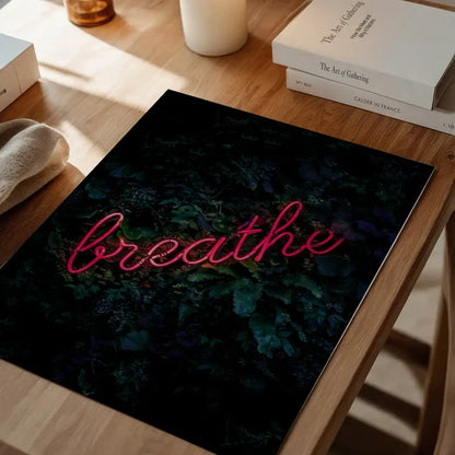 Breathe" neon style graphic print on dark foliage background, displayed on a wooden table.
