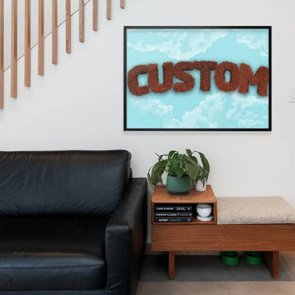 Framed brown fur-style "CUSTOM" text on a blue sky with clouds background, hanging above a black sofa.