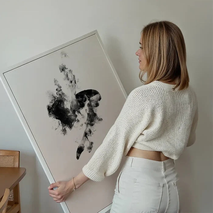 Woman holding a framed abstract print with dark, smoky shapes on a light background.