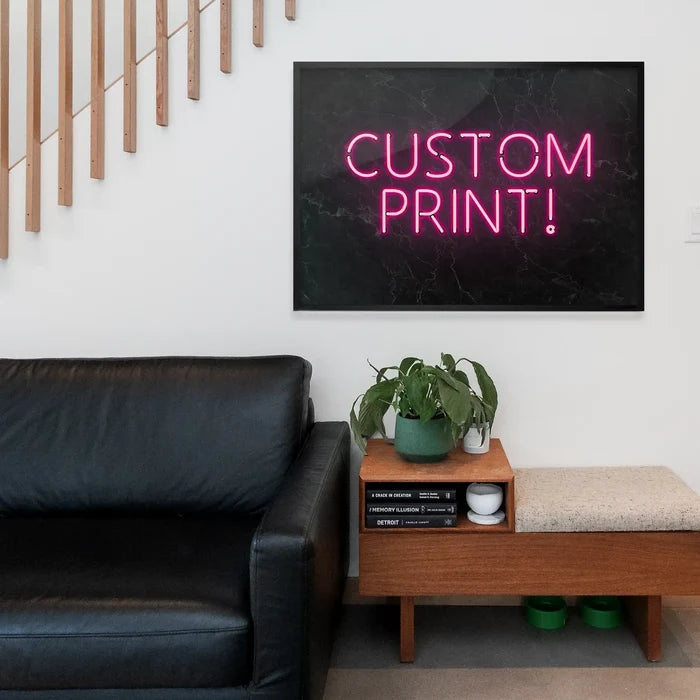 Pink neon "CUSTOM PRINT!" text on a black marble background, framed and hanging above a modern wooden bench.