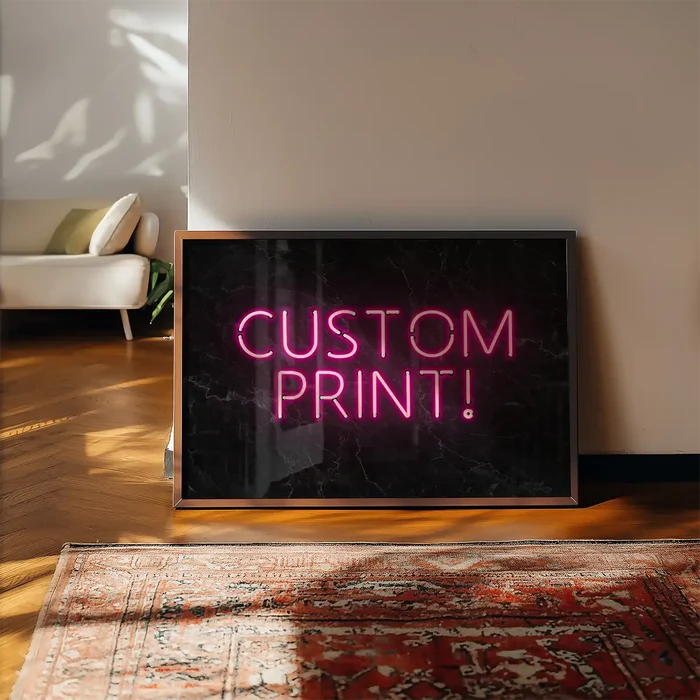 Custom neon sign print with pink "CUSTOM PRINT!" text on a black marble background, framed and leaning on a wall.