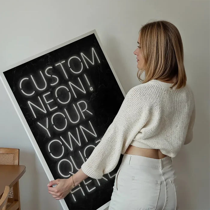 Woman holding a large framed custom quote poster print with white neon-style lettering on a dark background.