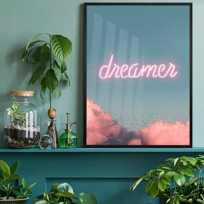 Framed "dreamer" neon print with pink clouds and birds against a blue sky, displayed on a green shelf with plants.