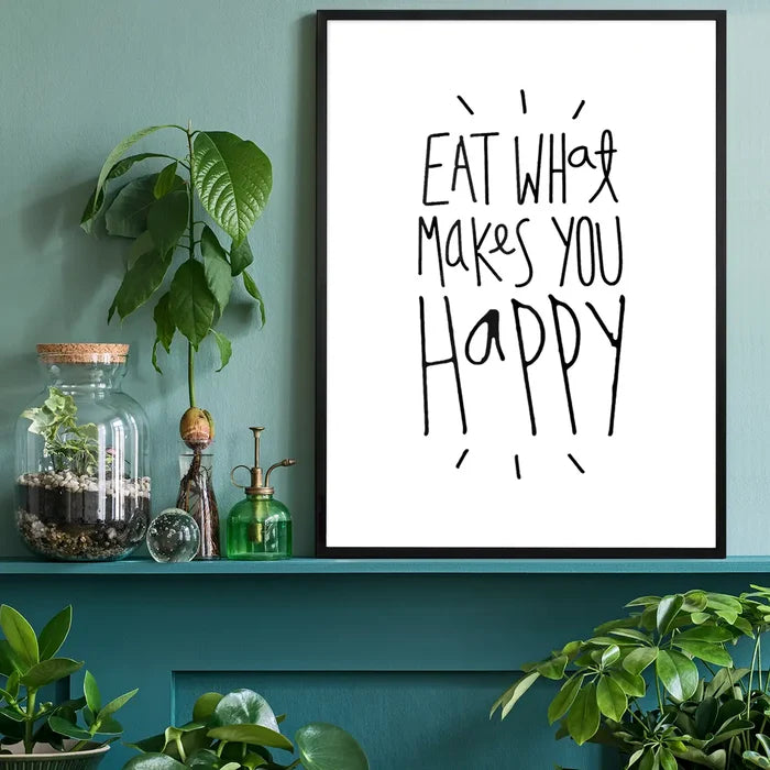 Black framed "Eat What Makes You Happy" typographic print on white paper, displayed on a green shelf.