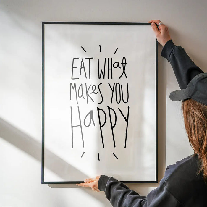 Framed "Eat What Makes You Happy" typographic print on white archival paper, held by hands.