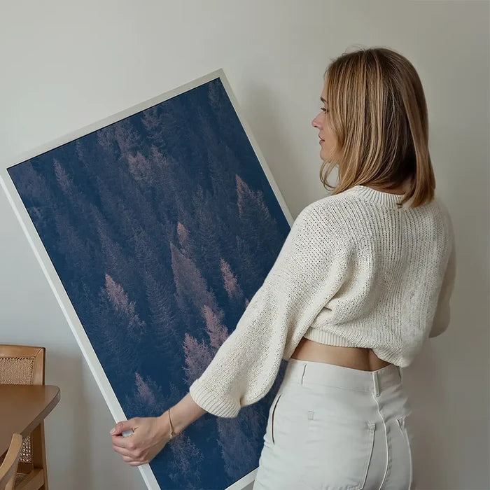 Woman holding a large framed forest print with blue and pink color shift on archival art paper.