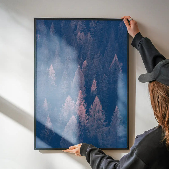 Framed forest print with blue and pink color shift, held by hands against a white wall.