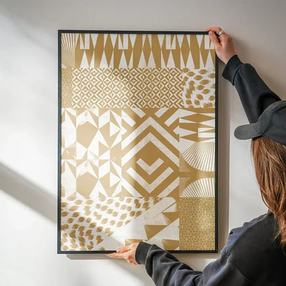 Hands hanging a framed gold and white abstract geometric pattern art print on a white wall.