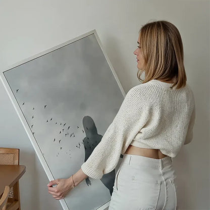 Graphic print of a female silhouette with a flock of birds against a subtle, grey sky.