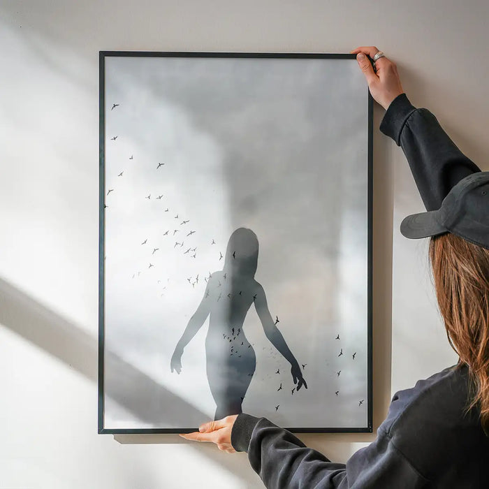 Monochrome graphic print of a female silhouette with a flock of birds, held in a black frame against a white wall.