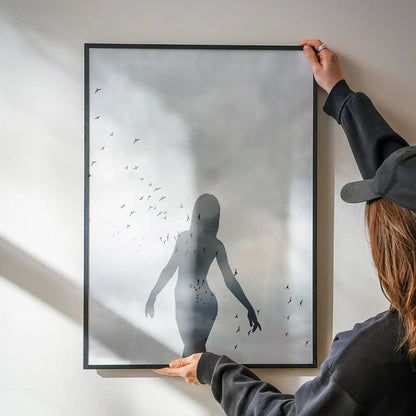 Monochrome graphic print of a female silhouette with a flock of birds, held in a black frame against a white wall.