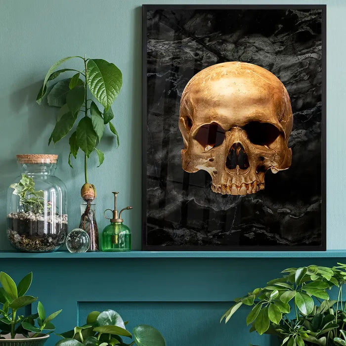 Gold skull art print on black marble background, framed and displayed on a shelf with plants.