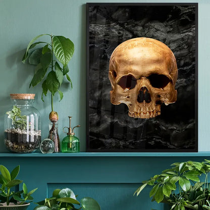 Gold skull art print on black marble background, framed and displayed on a shelf with plants.
