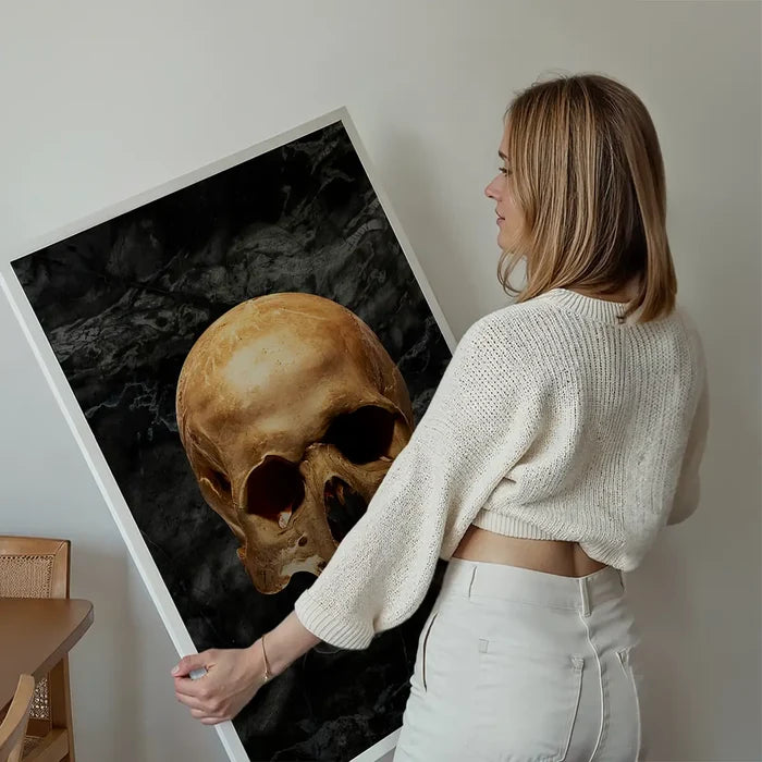 Woman holding a striking gold skull print on dark marble background, framed in white.