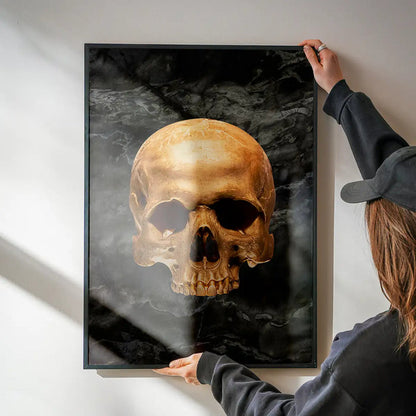 Gold skull on dark marble print in a black frame, held by hands.