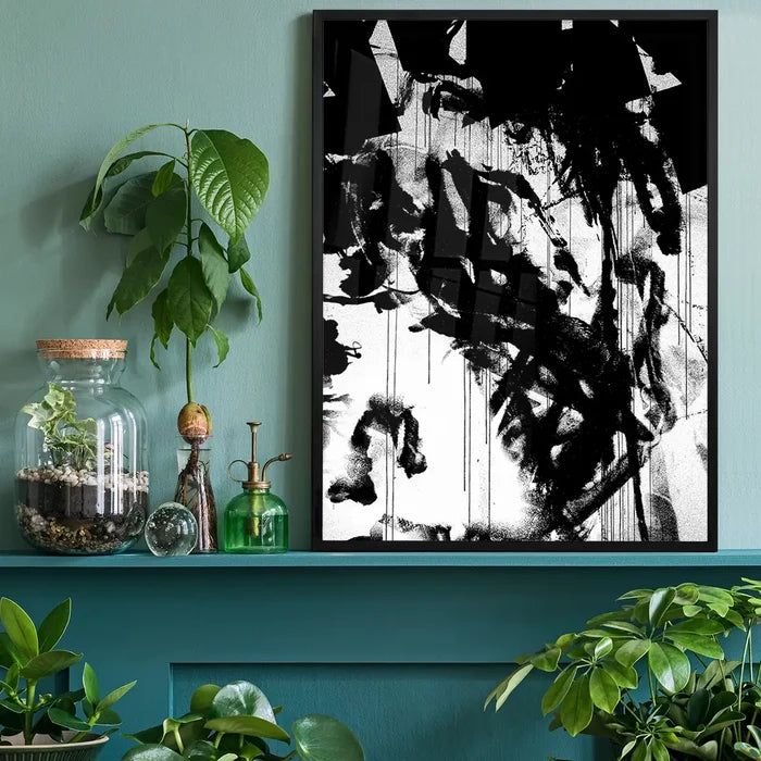 Black and white abstract graffiti art print in a black frame, displayed on a teal shelf with plants.