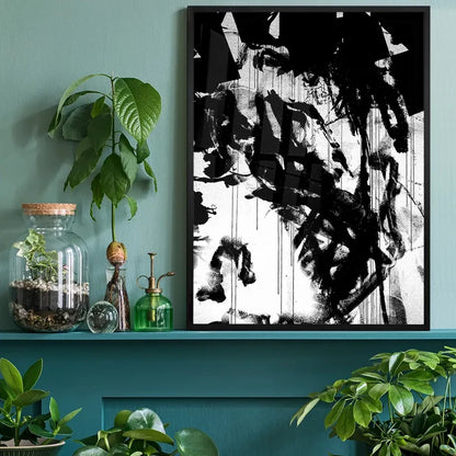 Black and white abstract graffiti art print in a black frame, displayed on a teal shelf with plants.