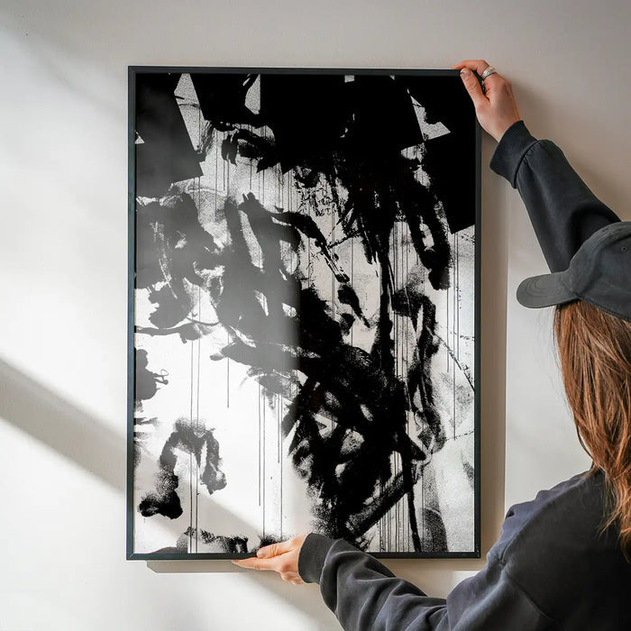 Abstract black and white graffiti art print with paint marks in a black frame, held by hands.