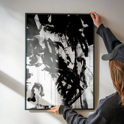 Abstract black and white graffiti art print with paint marks in a black frame, held by hands.