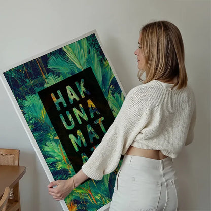 Blonde woman holding a framed Hakuna Matata tropical print with green palm leaves and colorful text.