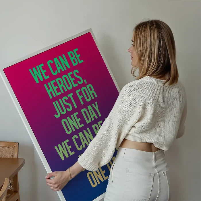 Woman holding a vibrant "Heroes" lyrics print with a pink-purple-blue gradient and neon green text.