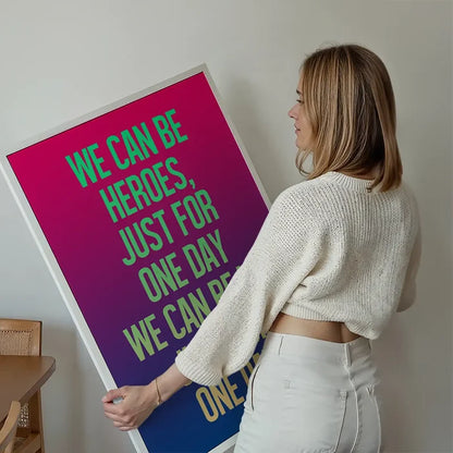 Woman holding a vibrant "Heroes" lyrics print with a pink-purple-blue gradient and neon green text.