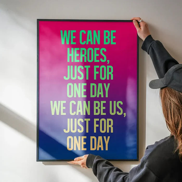 David Bowie "Heroes" lyrics print with neon green and yellow text on a vibrant pink to blue gradient background, held by hands.