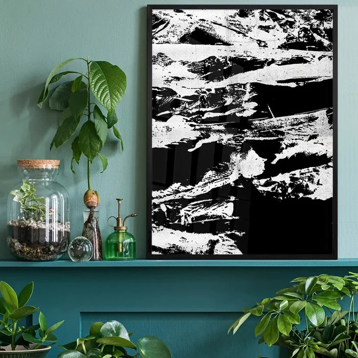 Black and white abstract graffiti print in a black frame, on a green wall above a shelf with plants.