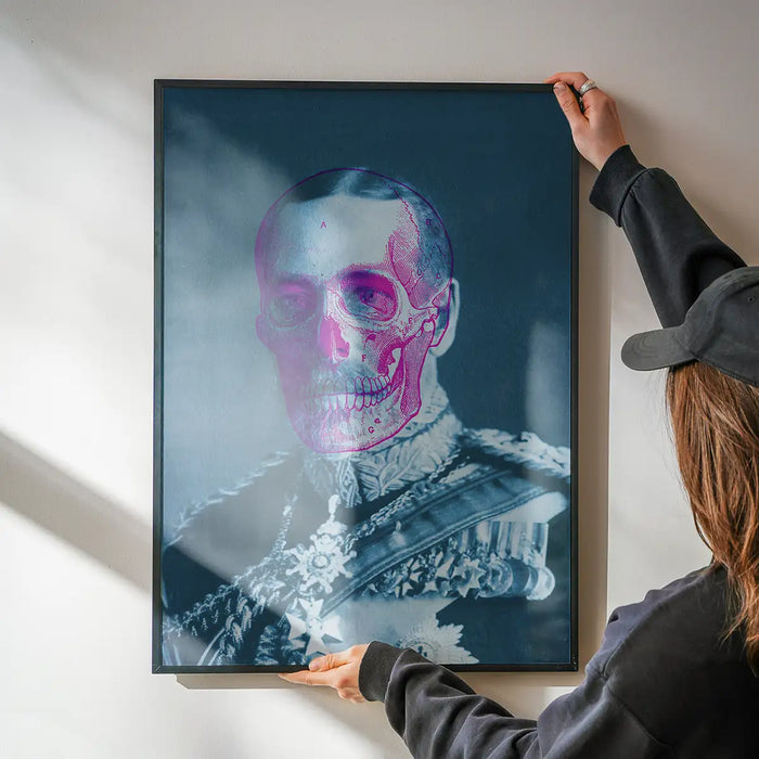 Urban art print of King George V with a pink skull overlay, held by hands against a white wall.