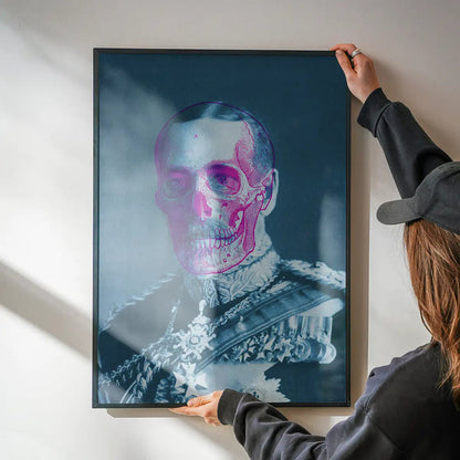 Urban art print of King George V with a pink skull overlay, held by hands against a white wall.