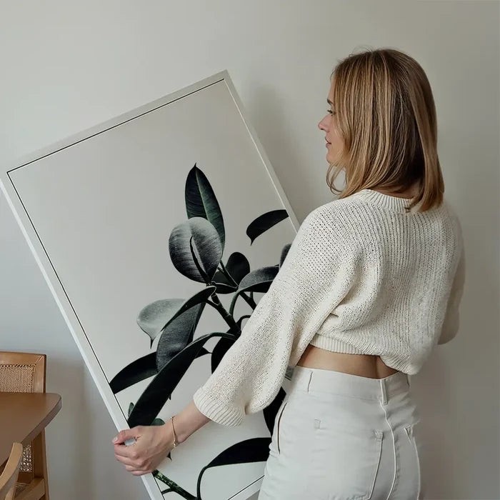 Woman holding a framed "Leaves Print" art with subtle green natural colors, ready to hang.