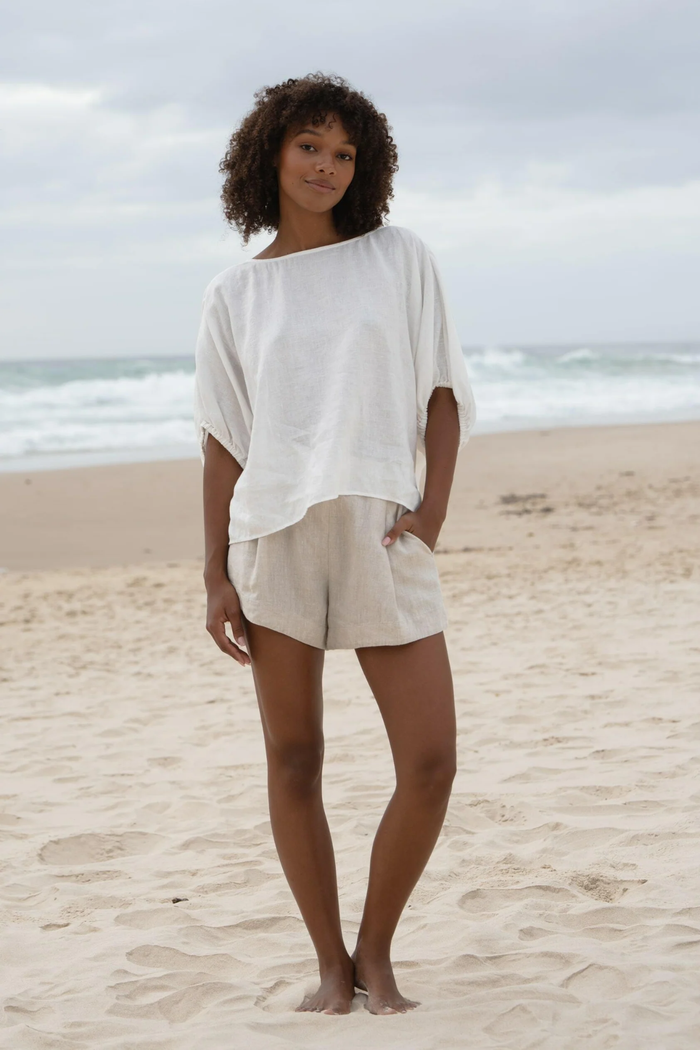 Woman wearing Lilly Pilly LPW23-T001 Tina Linen Top Ivory by Lilly Pilly standing on beach, shop Lilly Pilly at Dotique.