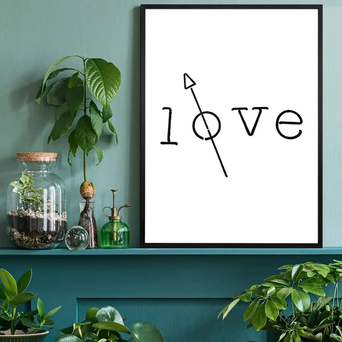 Black framed "love" typography print with arrow on white archival paper, displayed on a teal shelf.