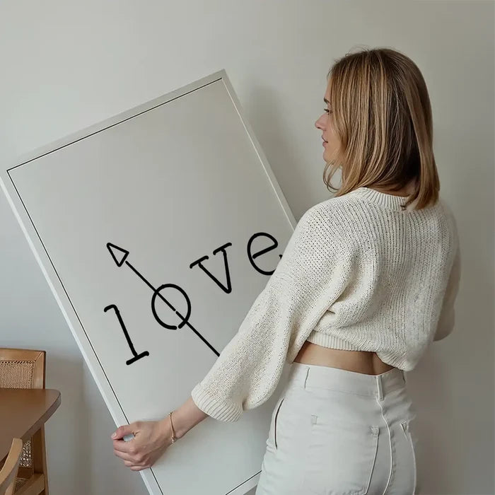 Woman holding a framed "love" typography print with a black arrow through the "o" on white archival paper.