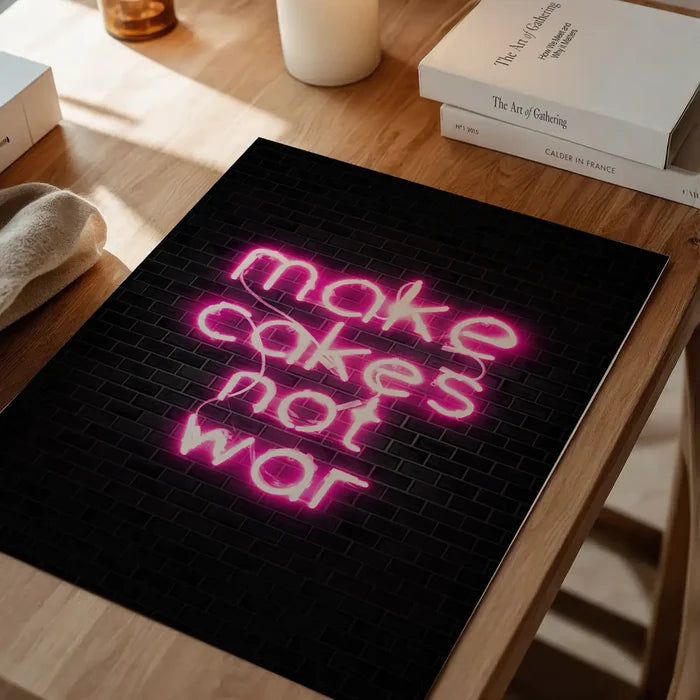 Pink neon "make cakes not war" print on black metro tile background, on a wooden table.
