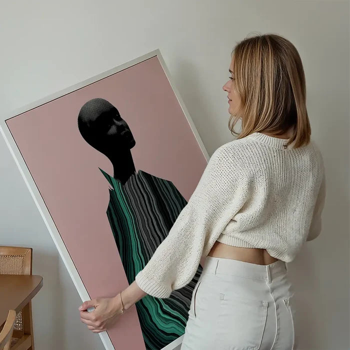 Woman holding a framed abstract female form art print with black and green marble textures on a pink background.