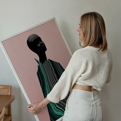 Woman holding a framed abstract female form art print with black and green marble textures on a pink background.