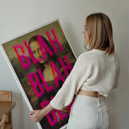 Woman holding a large framed "Moaning Mona Blah Blah Blah" print with pink typography overlay.