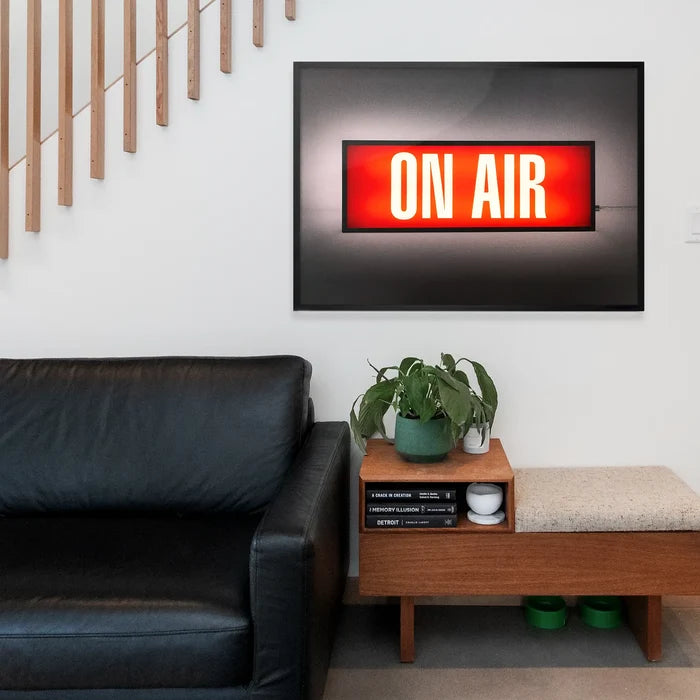 Retro "ON AIR" lightbox print in a black frame, hanging above a wooden bench and black leather sofa.