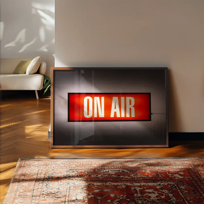 Retro "ON AIR" lightbox print on archival paper, framed, leaning against a wall on a wooden floor with a rug.