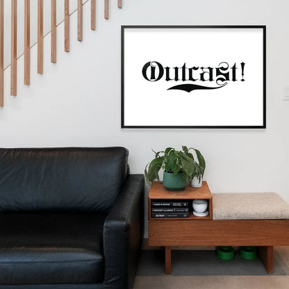 Black framed "Outcast!" typography print in a modern living room above a black leather sofa and wooden bench.