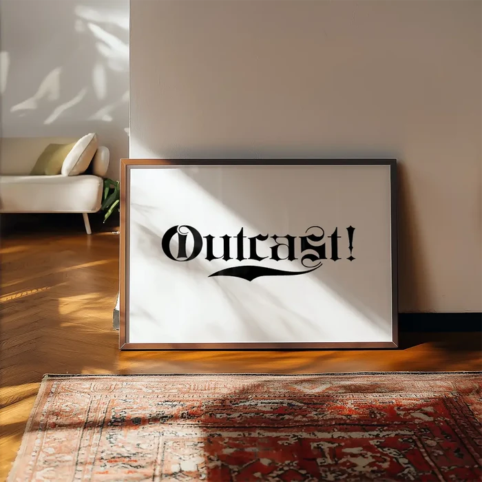 Framed "Outcast!" typography print with black text on white archival paper, leaning against a wall.
