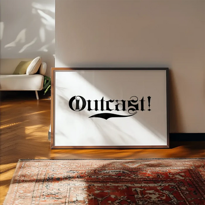 Framed "Outcast!" typography print with black text on white archival paper, leaning against a wall.