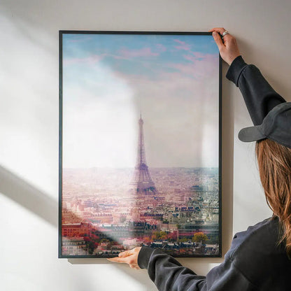 Framed Paris Eiffel Tower city photography print with abstract pink hue, held by hands against a white wall.