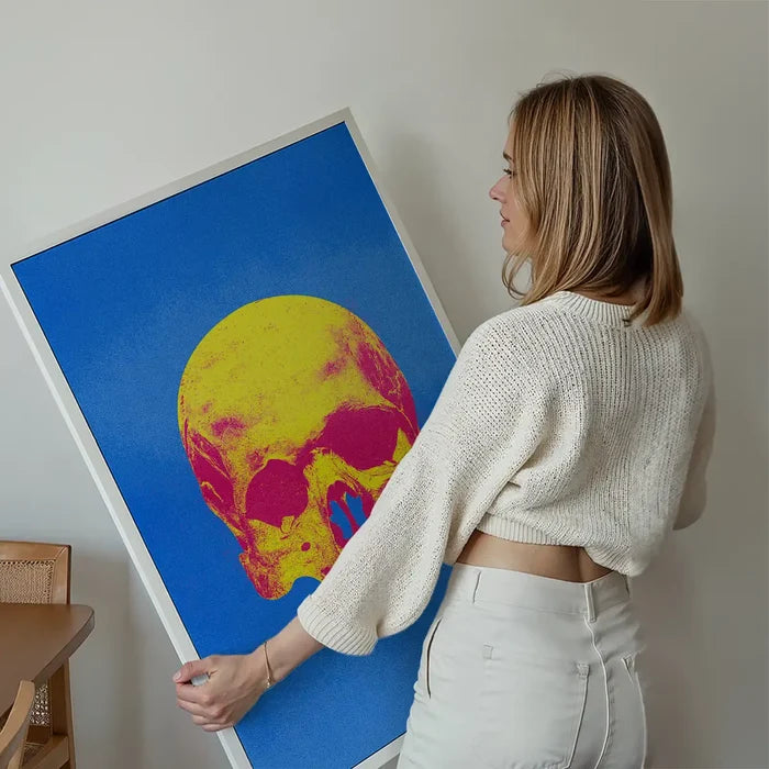 Woman holding a large framed Pop Art Warhol-style blue and yellow skull print on thick art paper.